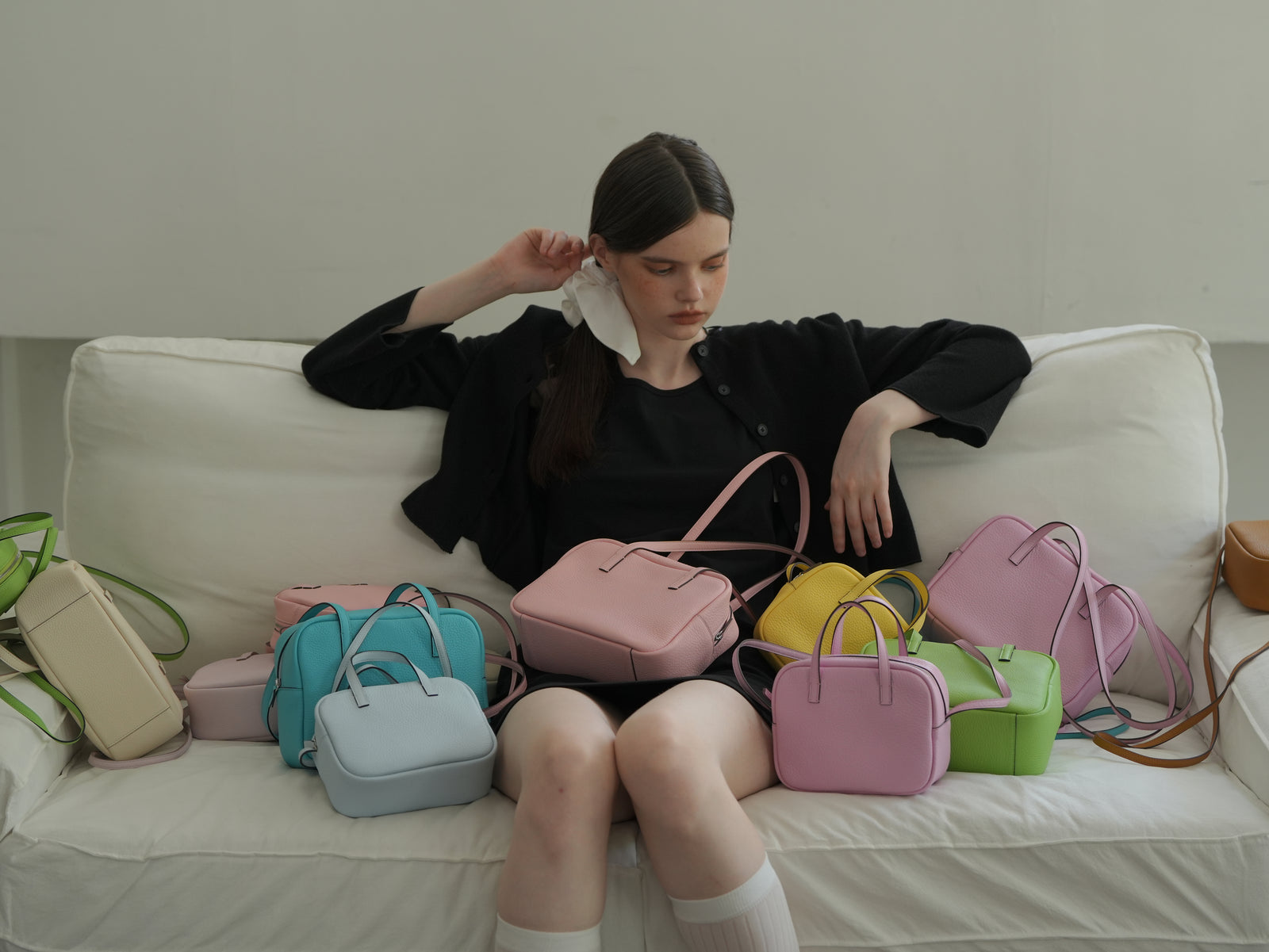 A collection of JOCQUELINE bags in many colors on a white sofa
