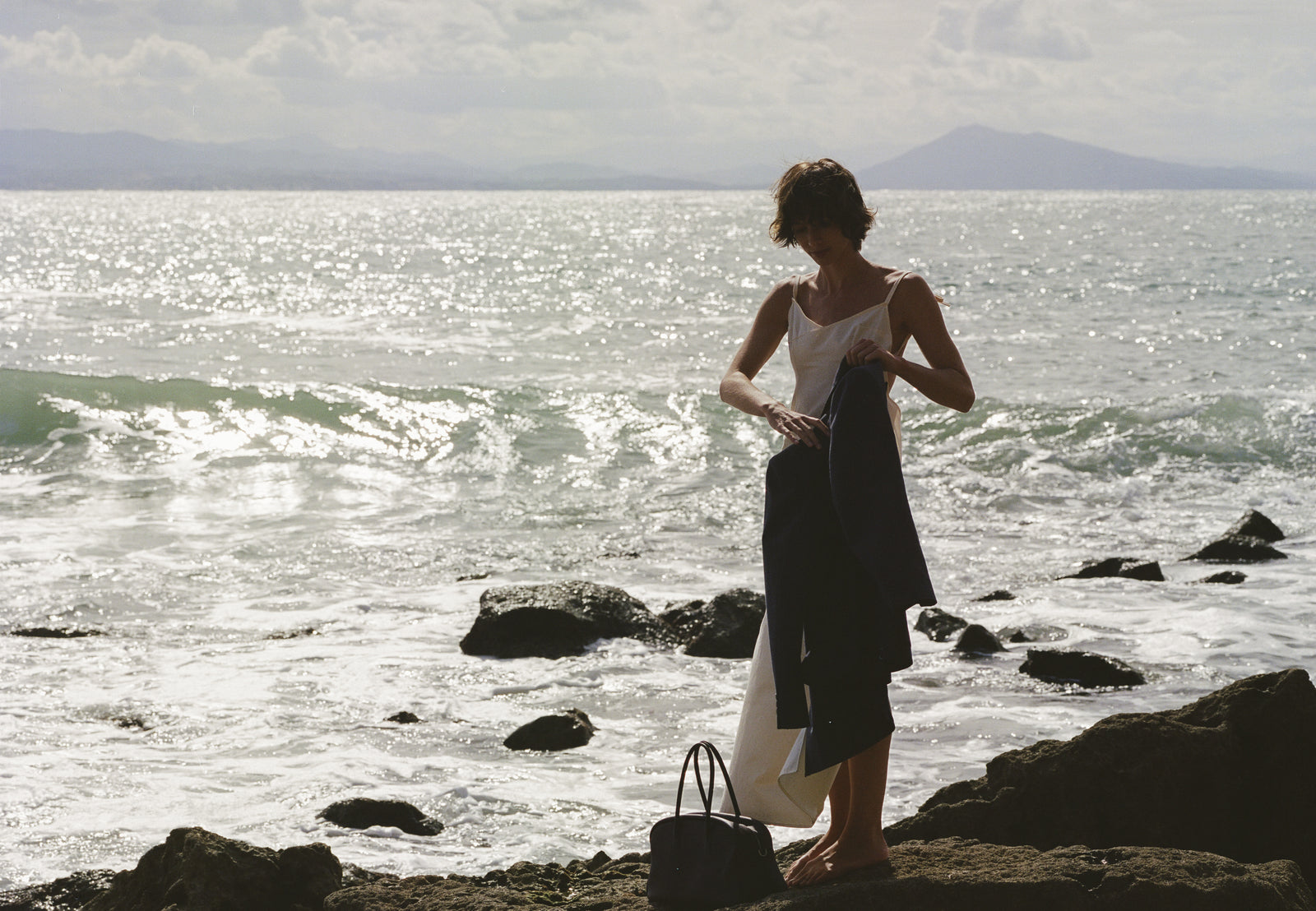 A woman on the rocks by the sea with a LUMA bag