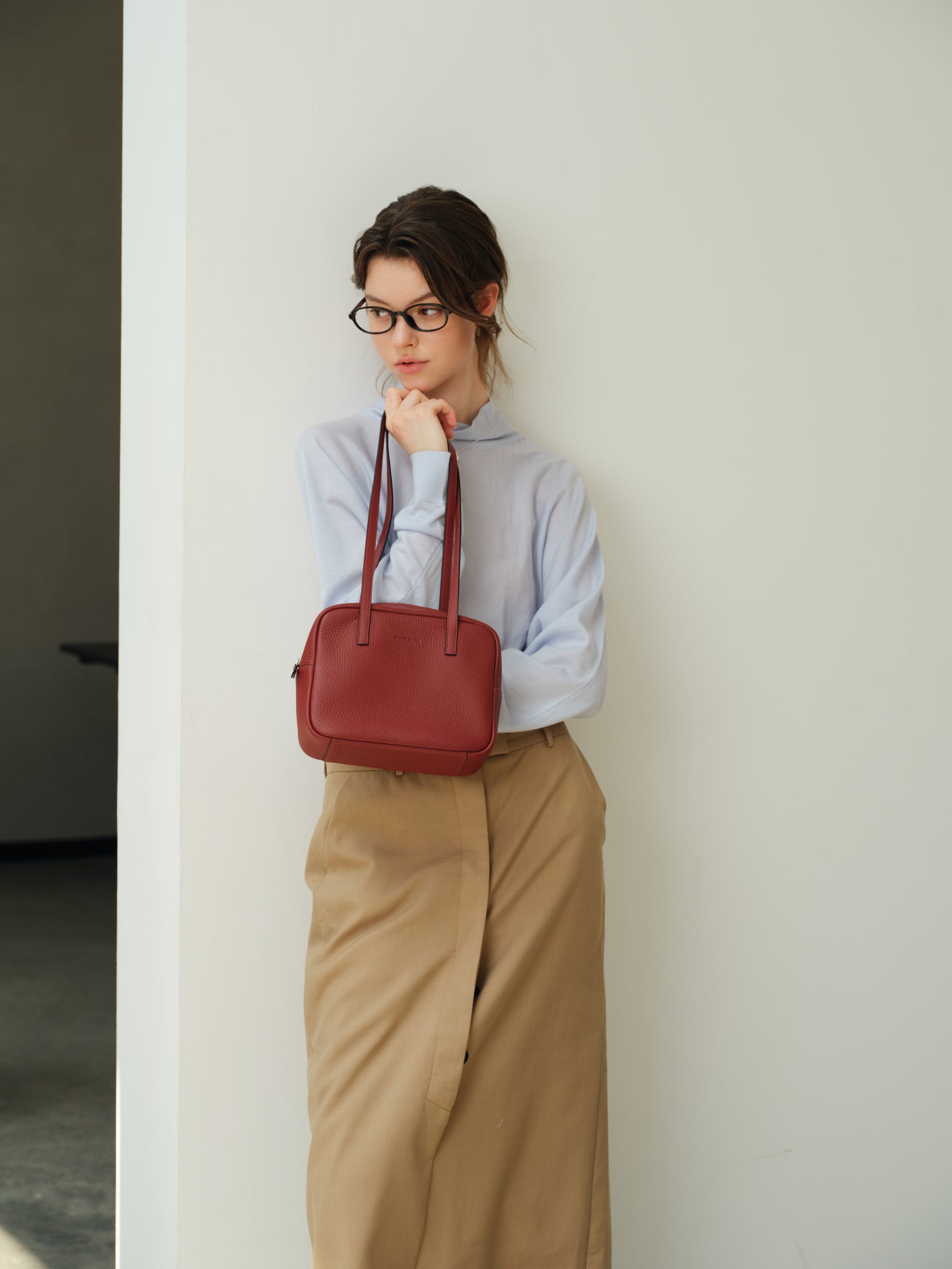 Woman leaning on a white wall with a red leather JOCQUELINE bag