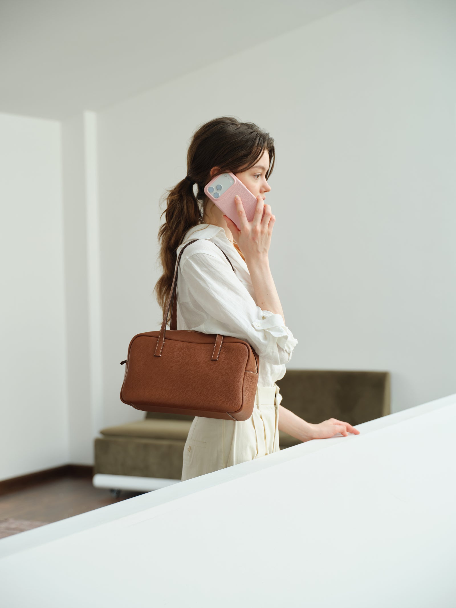 Woman on the phone with a pink JOCQUELINE case, a brown leather bag on her shoulder